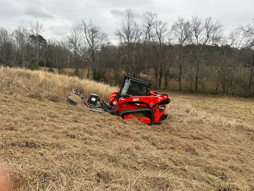 Red track loader with a brush cutter in a tall overgrown pasture, bush hogging