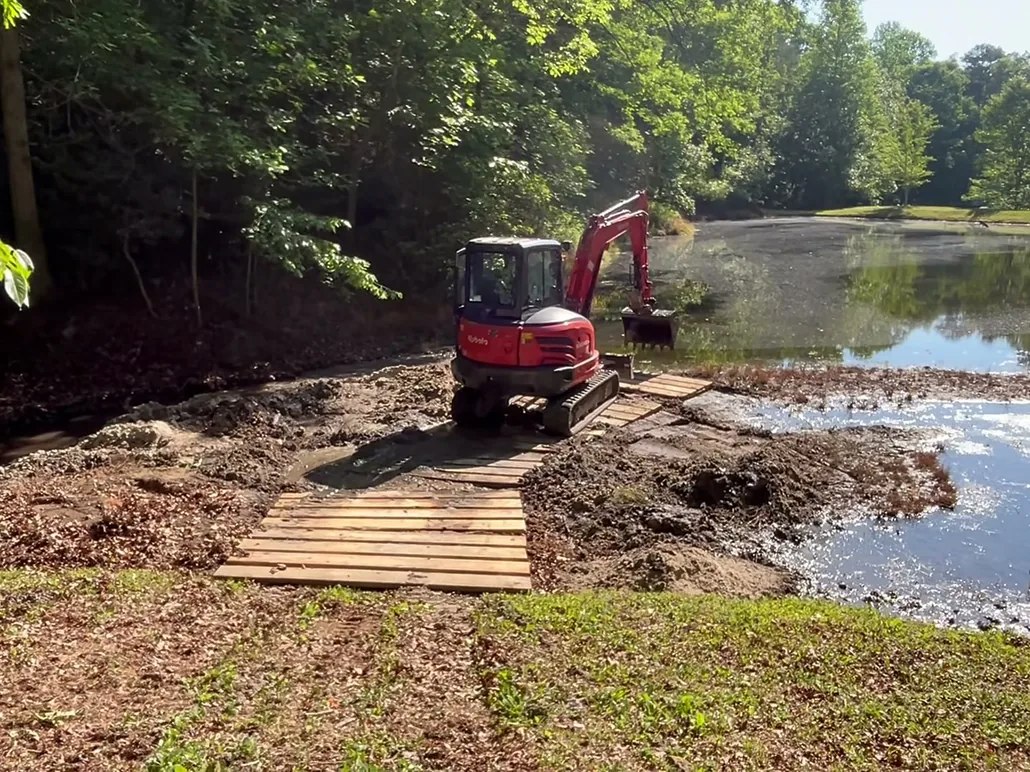 Mini excavator on timber mats cleaning silt out of a pond, excavation