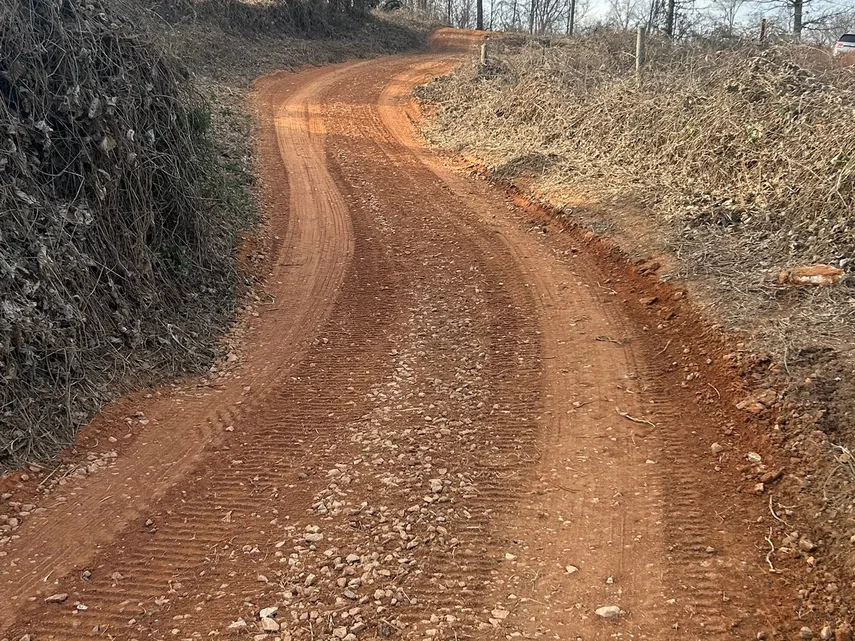 Red clay drive graded smooth along a wooded bank, land grading